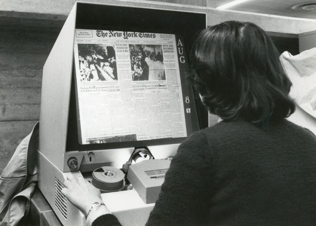 En person läser en tidning på microfilm med hjälp av en microfilmläsare.